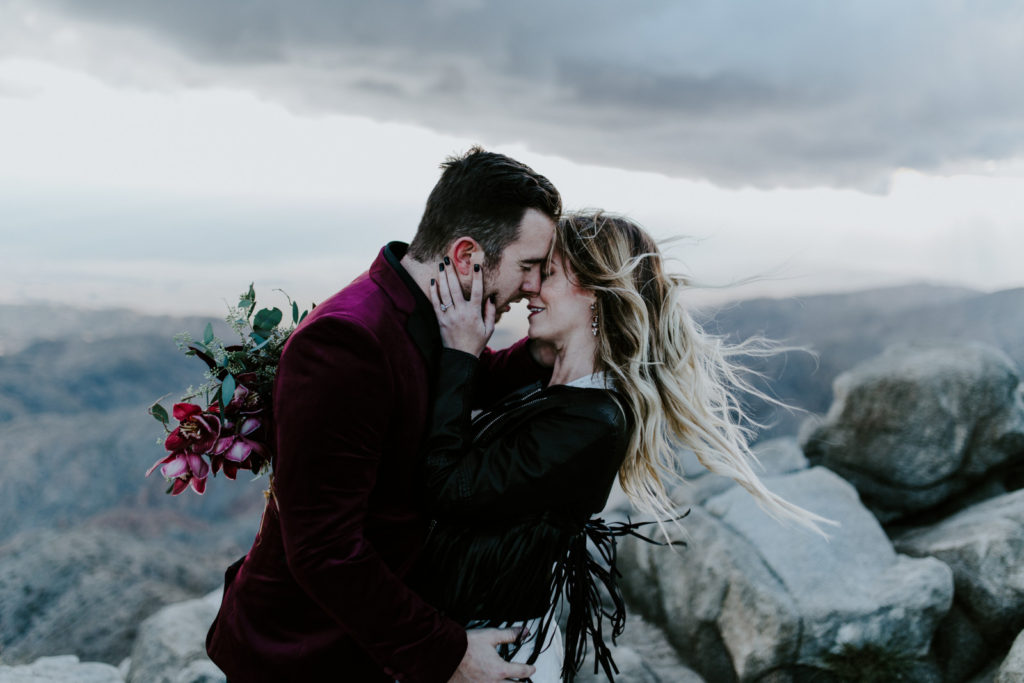 Alyssa and Jeremy go in for a kiss with Joshua Tree National Park in the background.