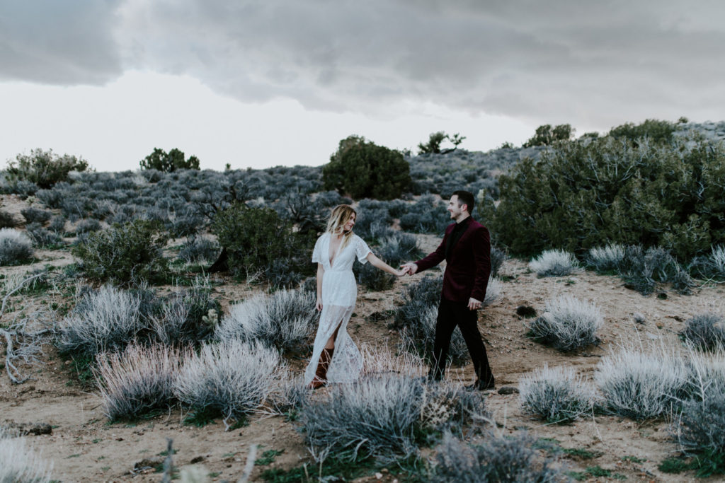 Alyssa and Jeremy walk hand in hand in the desert of Joshua Tree National Park.