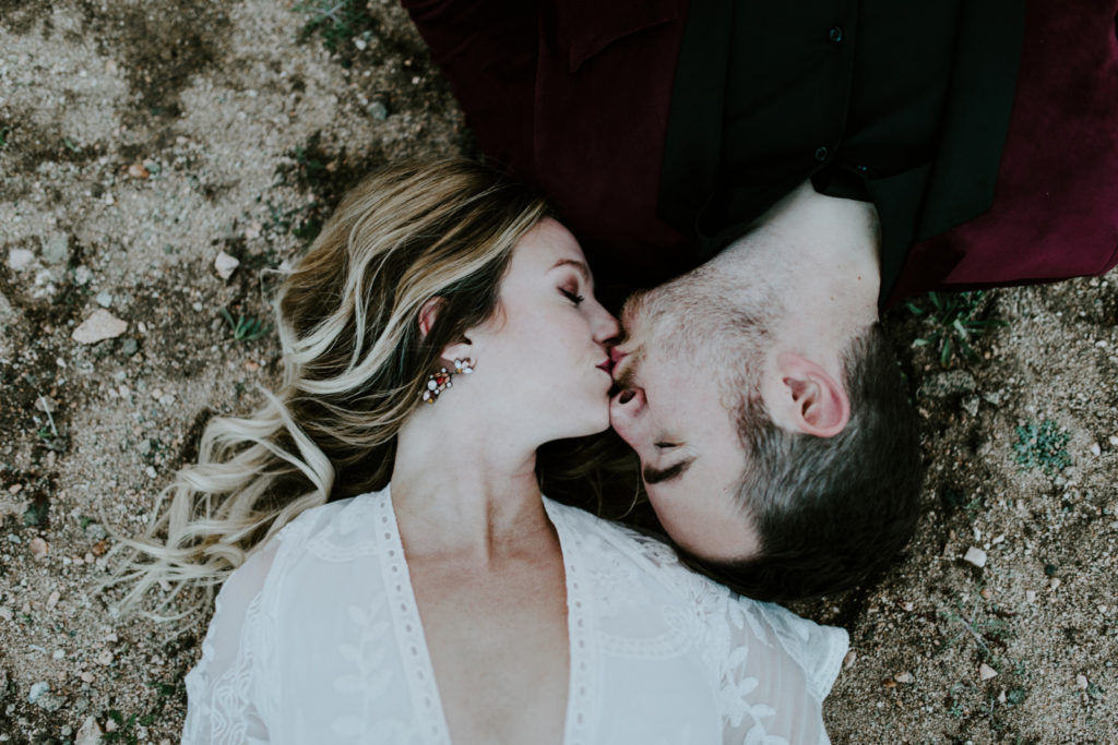 Jeremy and Alyssa kiss while laying in the sand in Joshua Tree National Park.